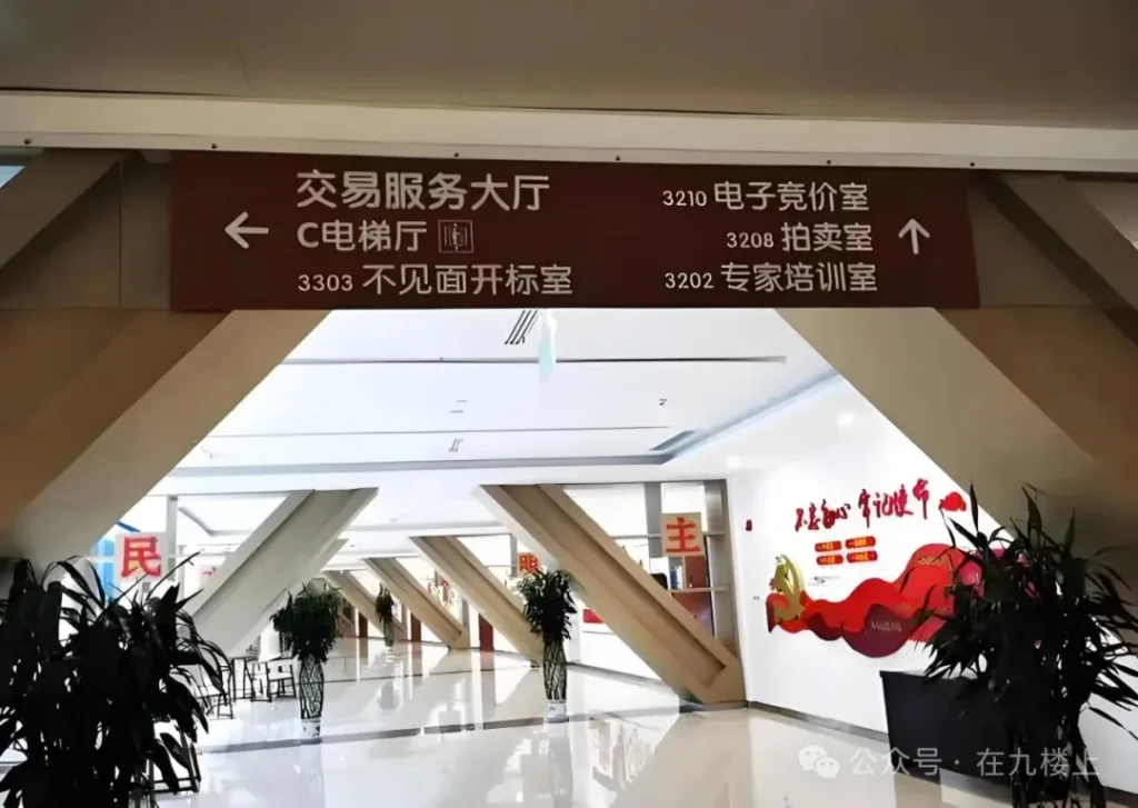 室内走廊的指示牌，显示多个房间和服务设施，包含电梯、电子竞价室、拍卖室等信息，环境明亮且现代化。