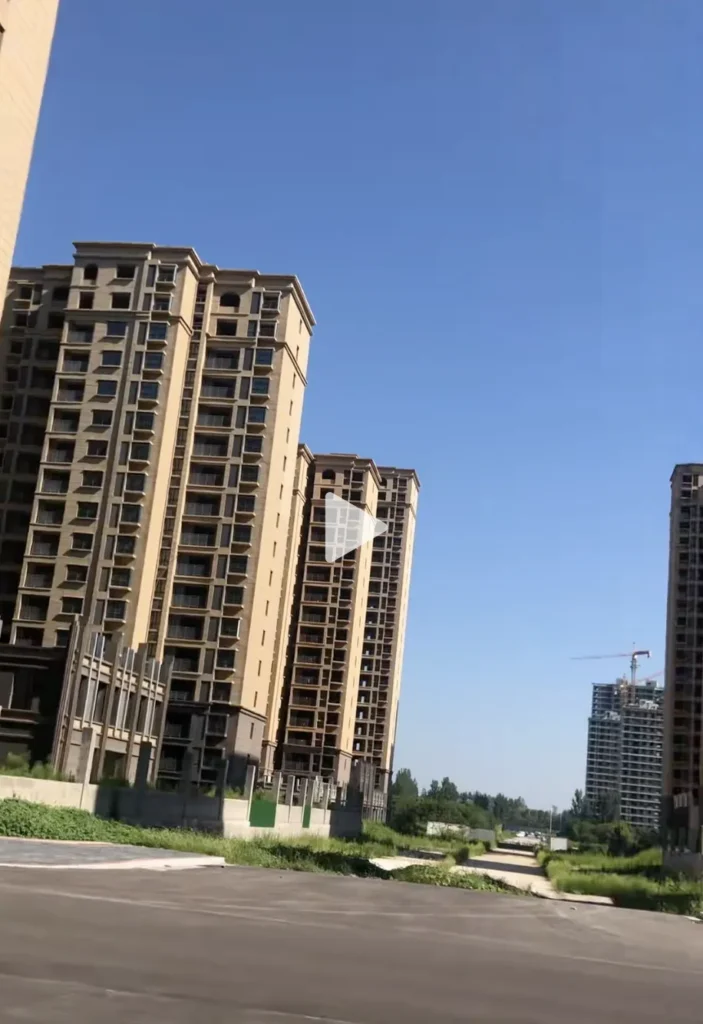 A view of tall, unfinished residential buildings under a clear blue sky, with a construction site visible in the background.
