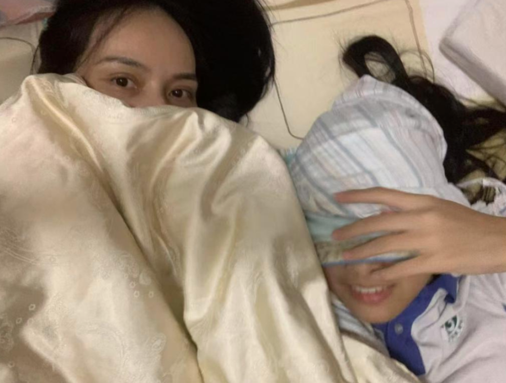 两人躺在床上一同使用毯子遮掩，面带微笑，表现出轻松的互动。