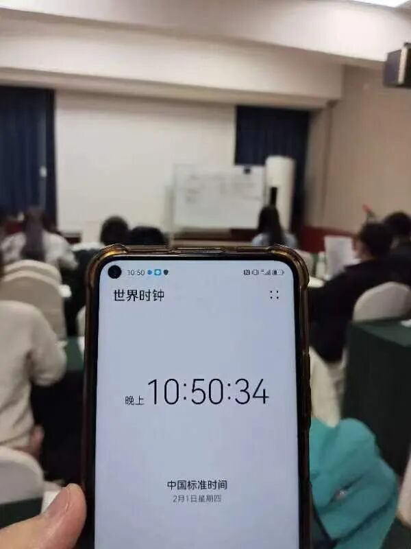 一只手 holding a smartphone 显示世界时间和中国标准时间，背景为一间教室，学生们坐在后面。